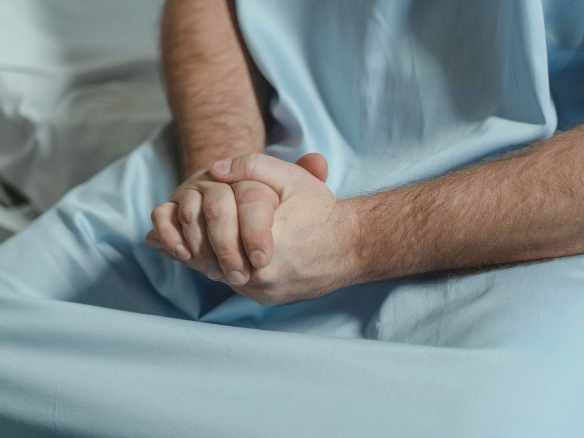 Gefaltete Hände eines Patienten als Symbol für Krankheit und existenzielle Belastung